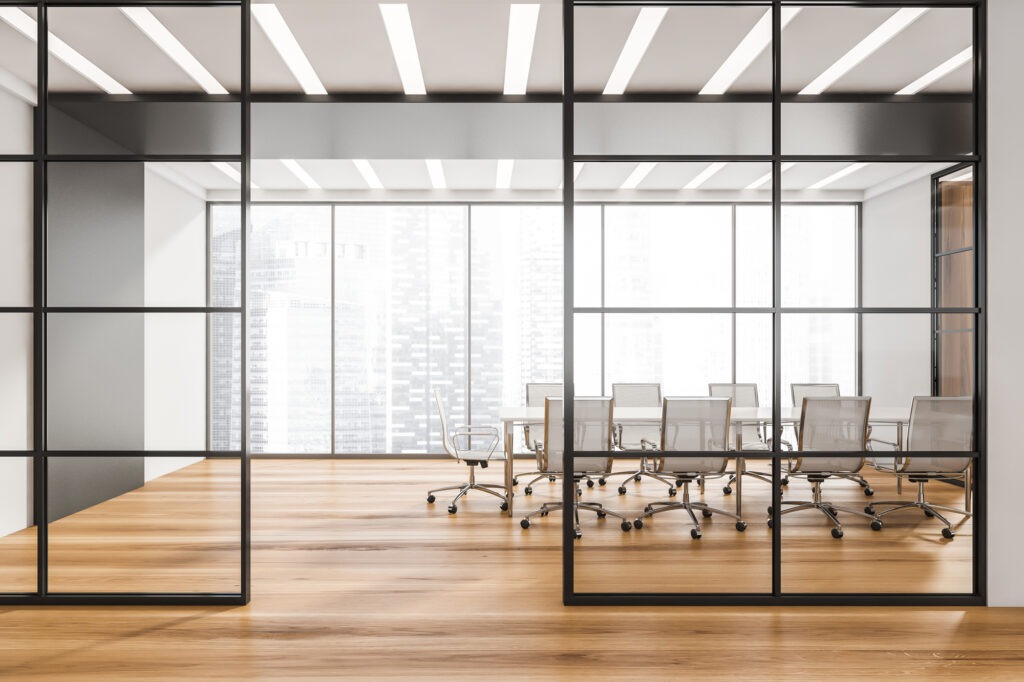 Corridor with half empty panoramic conference room behind the black framed glass wall partitions.